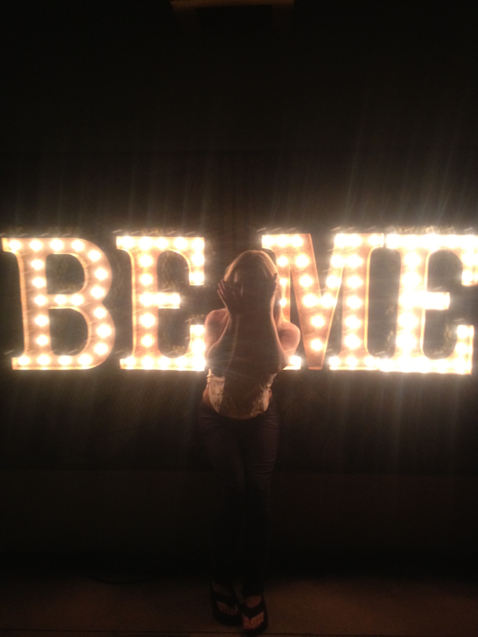 Jessica silhouetted before illuminated BELIEVE letters